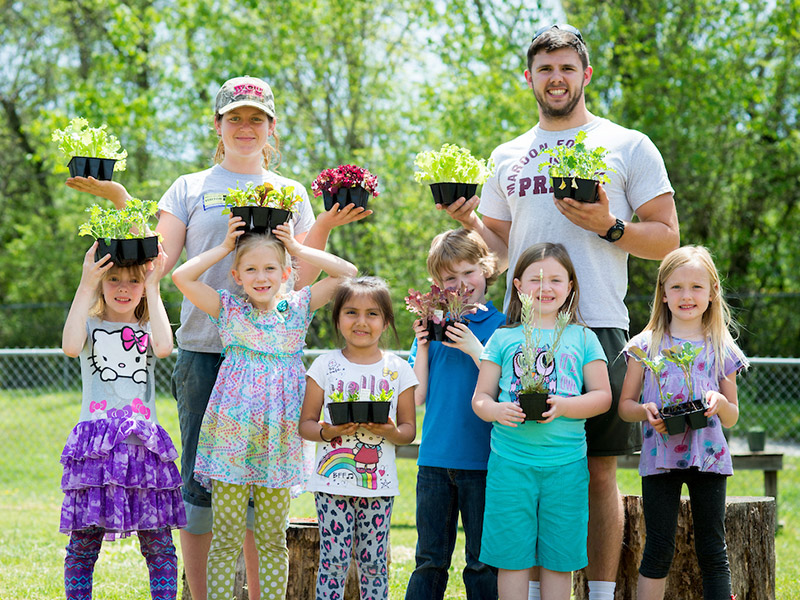 Photo of two adults and several children holding potted plants outside