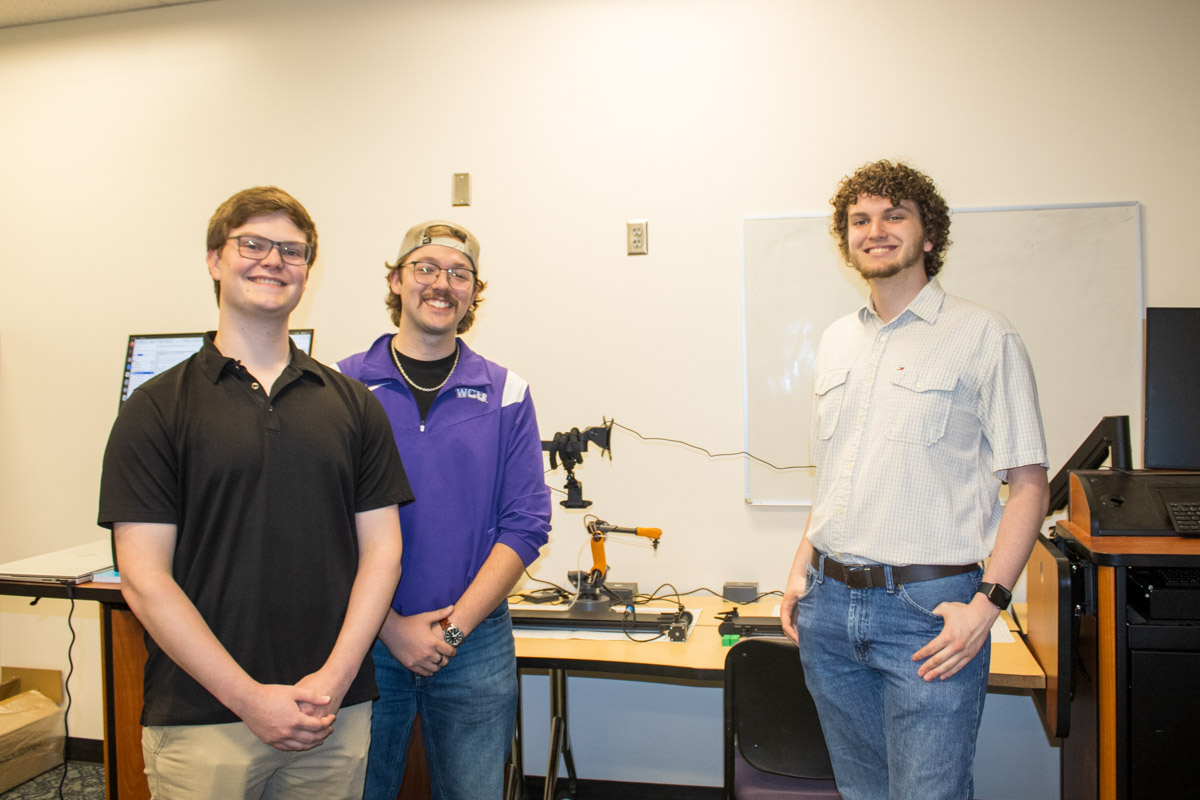 Three students on a team that worked with the Medusa robot are in group photo with the orange robot