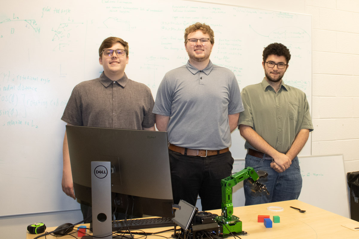 Three members of the Hulk robot student team stand with the green robot and a computer monitor