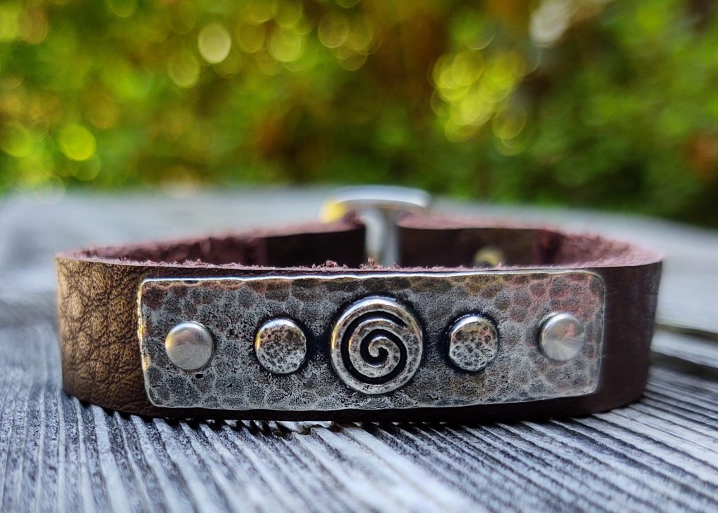 A brown leather bracelet with spiral metal and plain metal overplayed, hammered details.