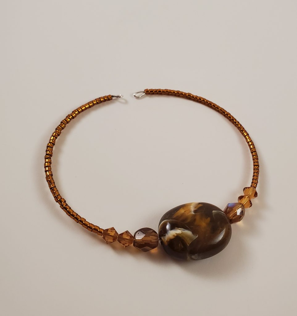 A brown square stone with rounded corners and white-is marbling sits in the center of a hand beaded bracelet