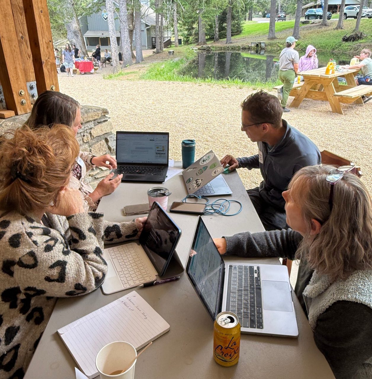 A group of engaged educators sitting around a picnic table with computers and papers